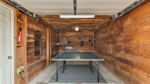 Ett bordtennisbord i ett rum med träpanel, en dörr, en brandsläckare och en hylla med diverse föremål.
