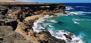Paisagem costeira com falésias rochosas e uma praia arenosa.