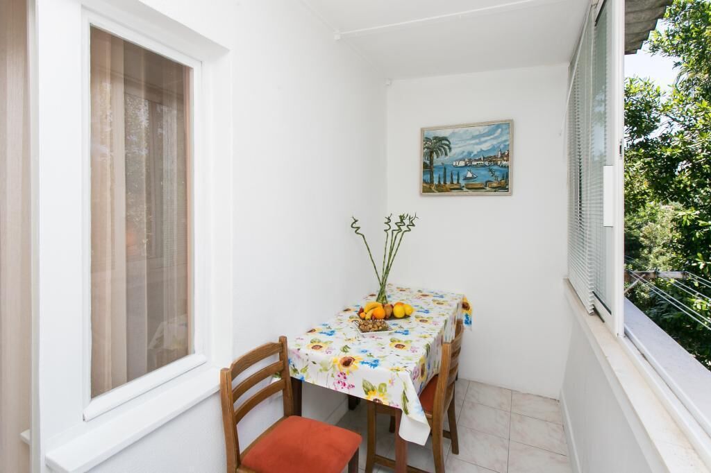 A small balcony with a table set for two, a painting on the wall, and a view of greenery.