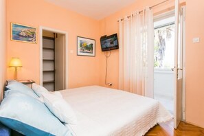 Un dormitorio con una cama, televisión, lámpara y puerta que da a un balcón.