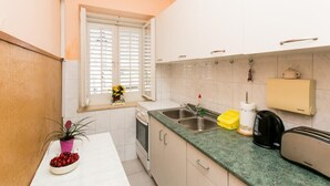 Une cuisine de taille réduite avec des meubles blancs, un plan de travail vert, un évier, une bouilloire et un grille-pain.