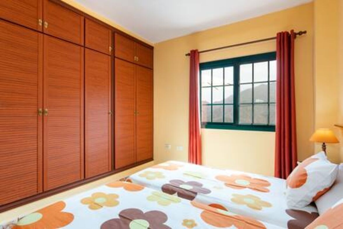 Une chambre à coucher avec un lit, une armoire en bois, une fenêtre avec des rideaux et une lampe.