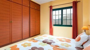 Un dormitorio con cama, armario de madera, ventana con cortinas y una lámpara.