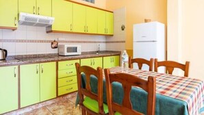Una cocina con gabinetes amarillos, un microondas blanco y una mesa con sillas.