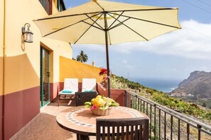 Un balcon avec une table, des chaises et un grand parasol.