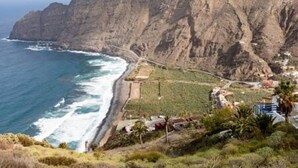 Un paisaje costero con un acantilado escarpado, una carretera a lo largo de la costa y algunos edificios con estructuras visibles.