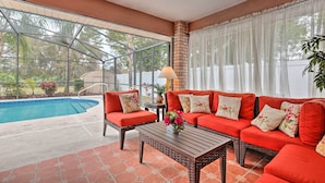 Eine sonnige Terrasse mit Pool, rotem Gartenmöbel und Blick ins Freie.