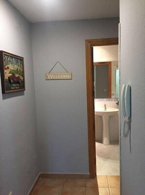 A hallway with a welcome sign, a framed Bugatti advertisement, and a bathroom visible through an open door.