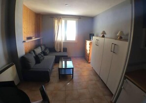 Un espacio habitable pequeño con sofá, una mesita de centro, un armario y una ventana con cortinas.