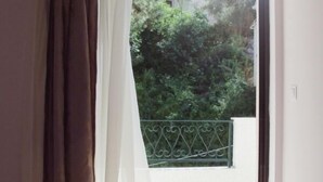A room with a bed, a window with curtains, and a view of greenery outside. - Yasemi Rooms (Lefkada)