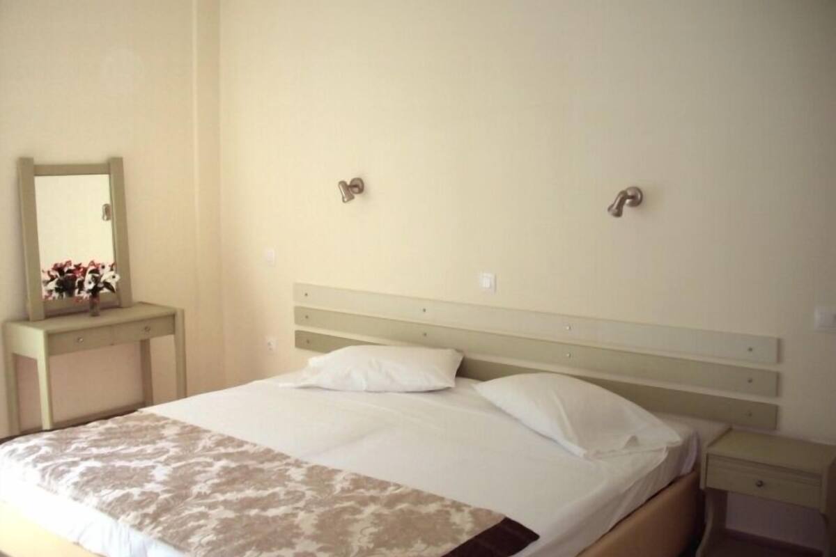 Hotellihuone, jossa on sänky, yöpöytä, lipasto ja peili.