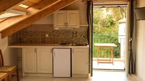 A compact kitchen with white cabinets, a small refrigerator, and a window leading to an outdoor patio. - Yasemi Rooms (Lefkada)