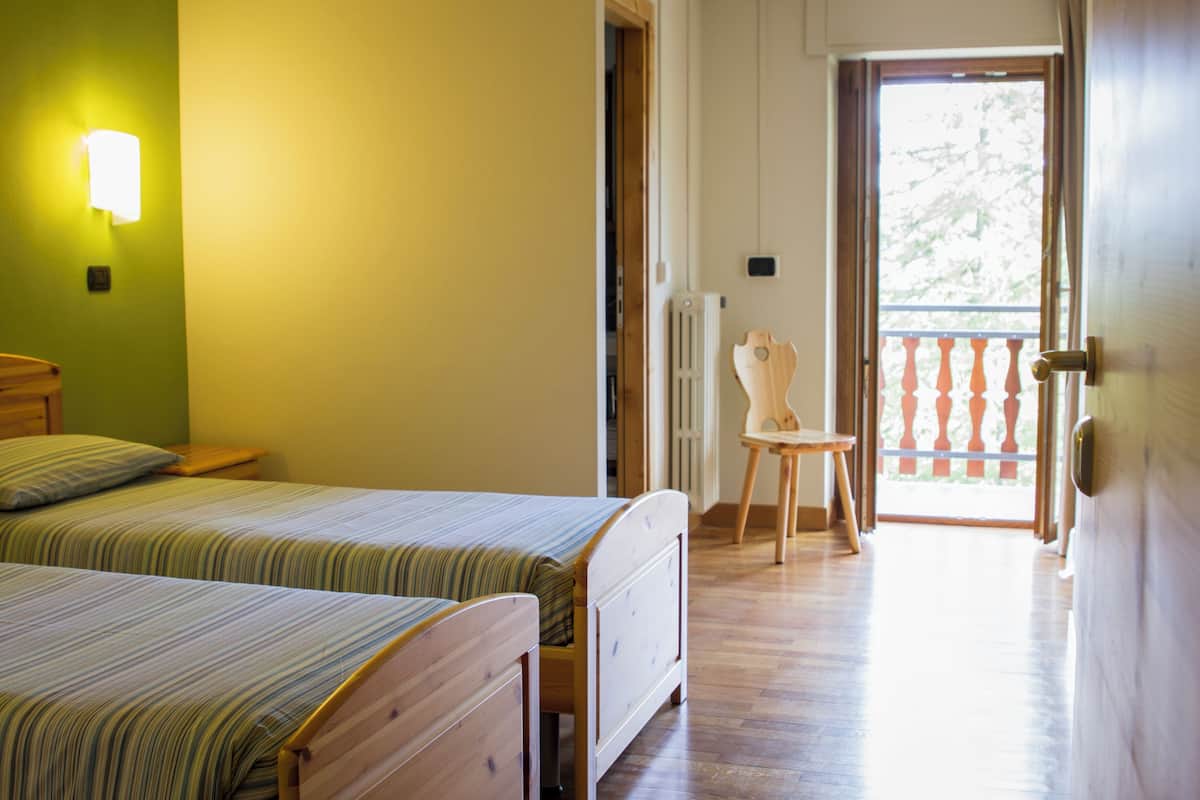 A bedroom with two beds, a wooden chair, a radiator, and a balcony with a railing.