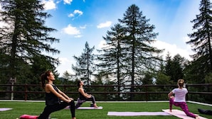 Three people practicing yoga on outdoor mats in a grassy area with trees in the background. - Albergo Ristorante Cuccini (Varzo)