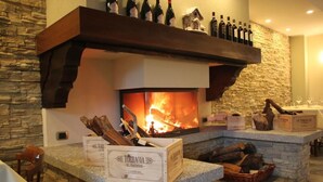 A stone fireplace with a fire, surrounded by logs and wine bottles. - Albergo Ristorante Cuccini (Varzo)