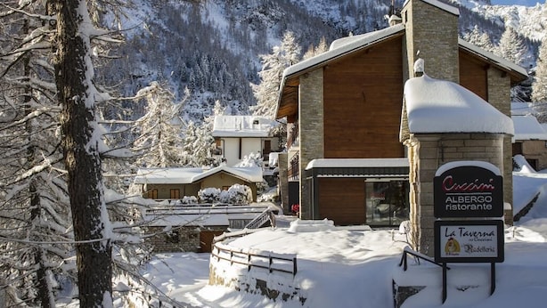 A rustic mountain lodge with a stone facade and wooden accents, surrounded by snow-covered trees and mountains. - Albergo Ristorante Cuccini (Varzo)