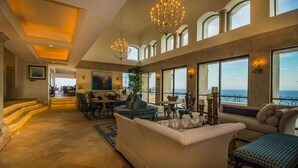 A spacious living area with a large sofa, a dining table, and multiple chairs. There are large windows offering a view of the ocean. - Exclusive Holiday Villa with Private Pool near Beach, Cabo San Lucas Villa 1042 (Cabo San Lucas)