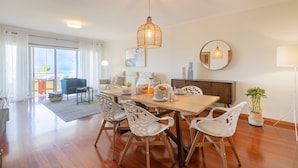 Uma área de refeições com uma mesa de madeira, cadeiras brancas e um lustre.