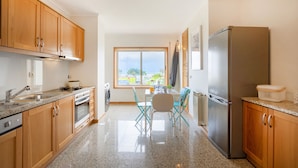 Uma cozinha com armários de madeira, geladeira de aço inoxidável, bancada de granito, janela com vista e área de jantar com mesa e cadeiras.