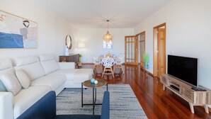 Sala de estar com sofá, mesa de centro, rack para TV e área de jantar com mesa e cadeiras.