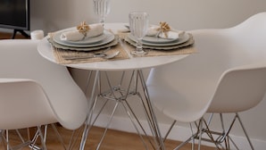 A dining area with a round mirror, framed artwork, and a table set for two.
