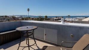 A rooftop terrace with a table and chairs, overlooking a coastal cityscape. - Beautiful Updated House with Ocean Views in Downtown Pismo (Pismo Beach)