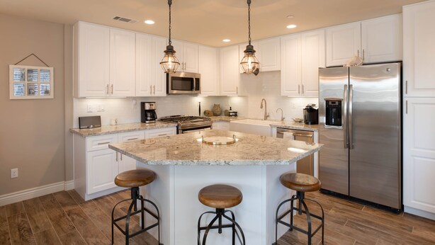 A modern kitchen with white cabinets, a stainless steel refrigerator, a granite island with stools, and pendant lighting. - Beautiful Updated House with Ocean Views in Downtown Pismo (Pismo Beach)
