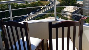 Un balcon avec deux chaises en bois et une vue sur une route côtière où circulent des voitures.
