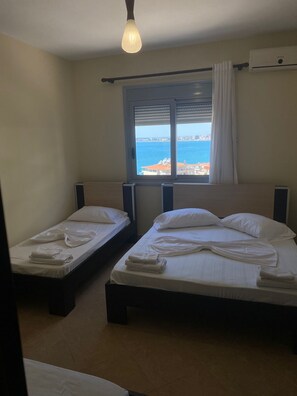 Una habitación con dos camas, una ventana vista al mar y una lámpara colgante.