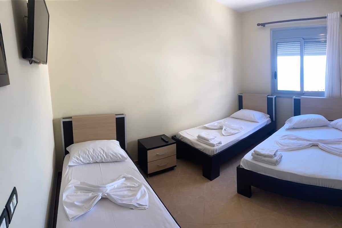 Quarto de hotel com duas camas de solteiro, uma pequena mesa de cabeceira com controle remoto e uma janela com persianas.