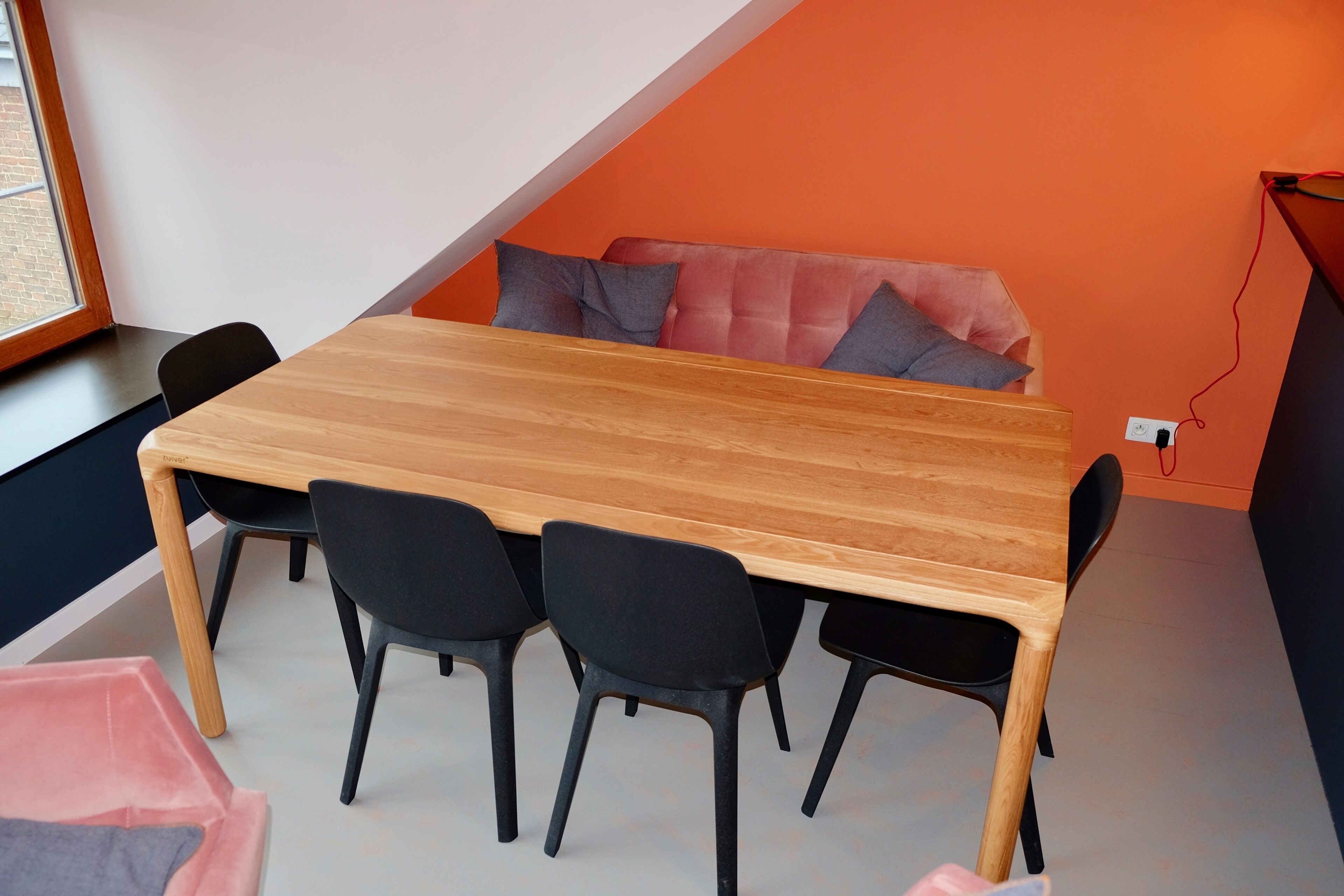 A modern room with a wooden table and black chairs, orange walls, and a window.