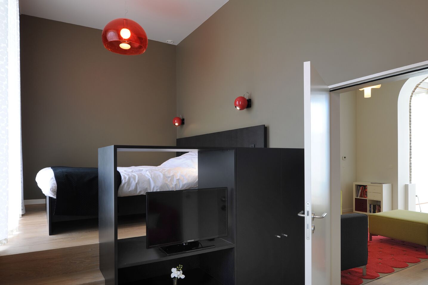 Un dormitorio moderno con una cama litera, un televisor de pantalla plana y una lámpara colgante roja.