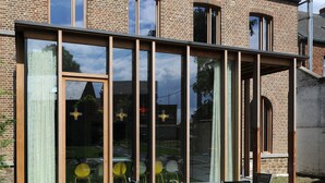A modern house with large windows and a patio area with chairs. - Le Presbytère (Engis)