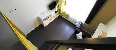 Un interior moderno con una escalera, una consola blanca, un televisor de pantalla plana y una lámpara colgante amarilla.