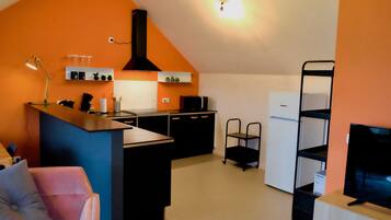 Een kleine keuken met een centraal eiland, zwarte kastjes en een witte koelkast.