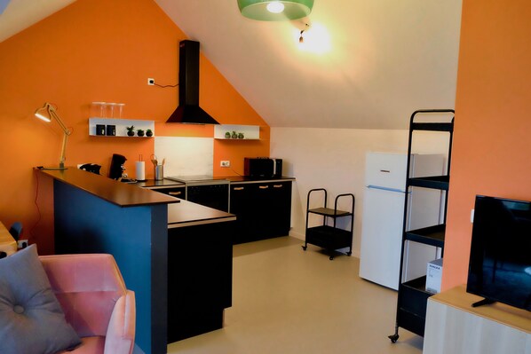 Una cocina compacta con una isla central, armarios negros y un refrigerador blanco.