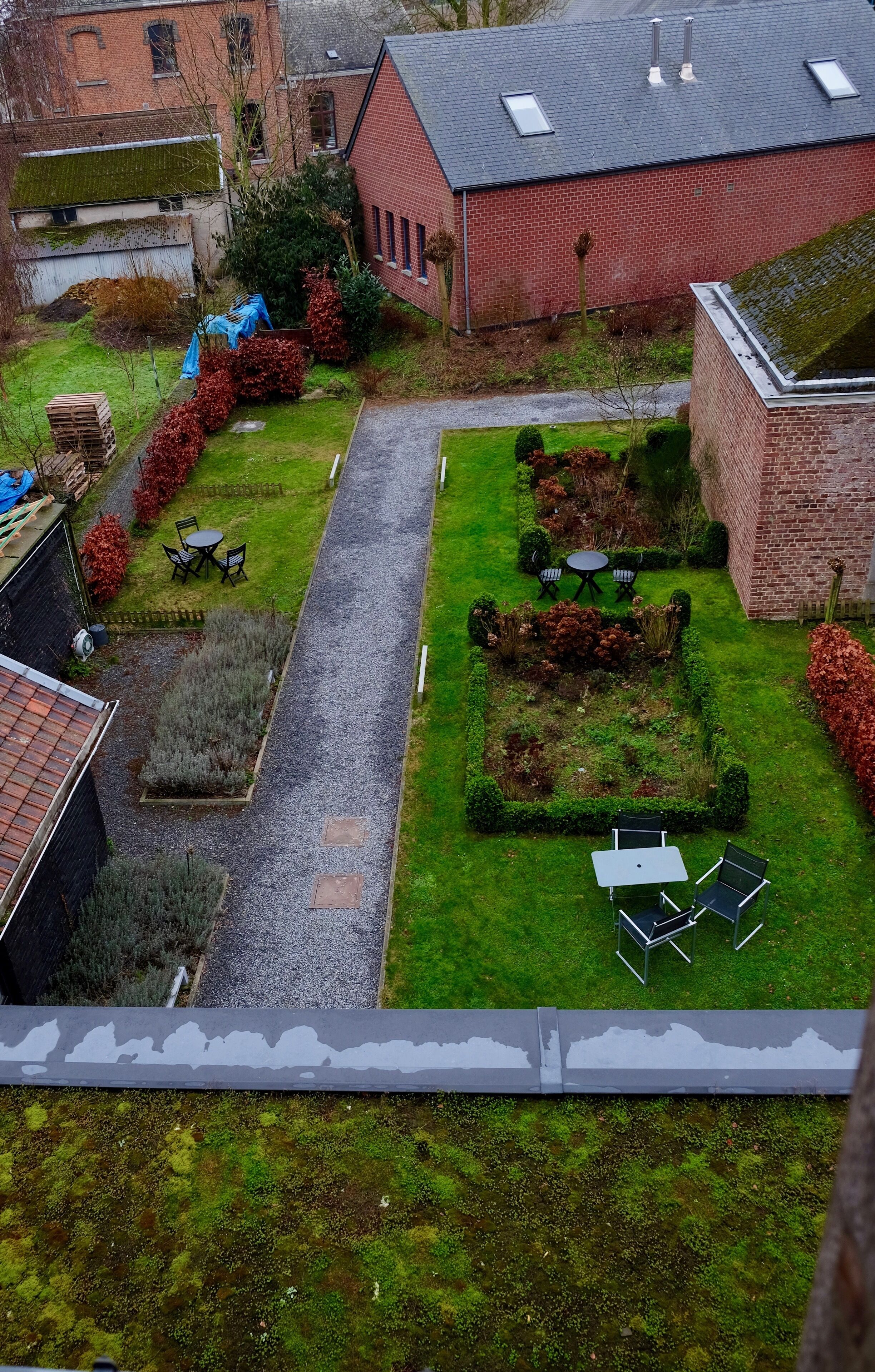 A courtyard with a gravel path, green lawns, and a brick building with a sloped roof.