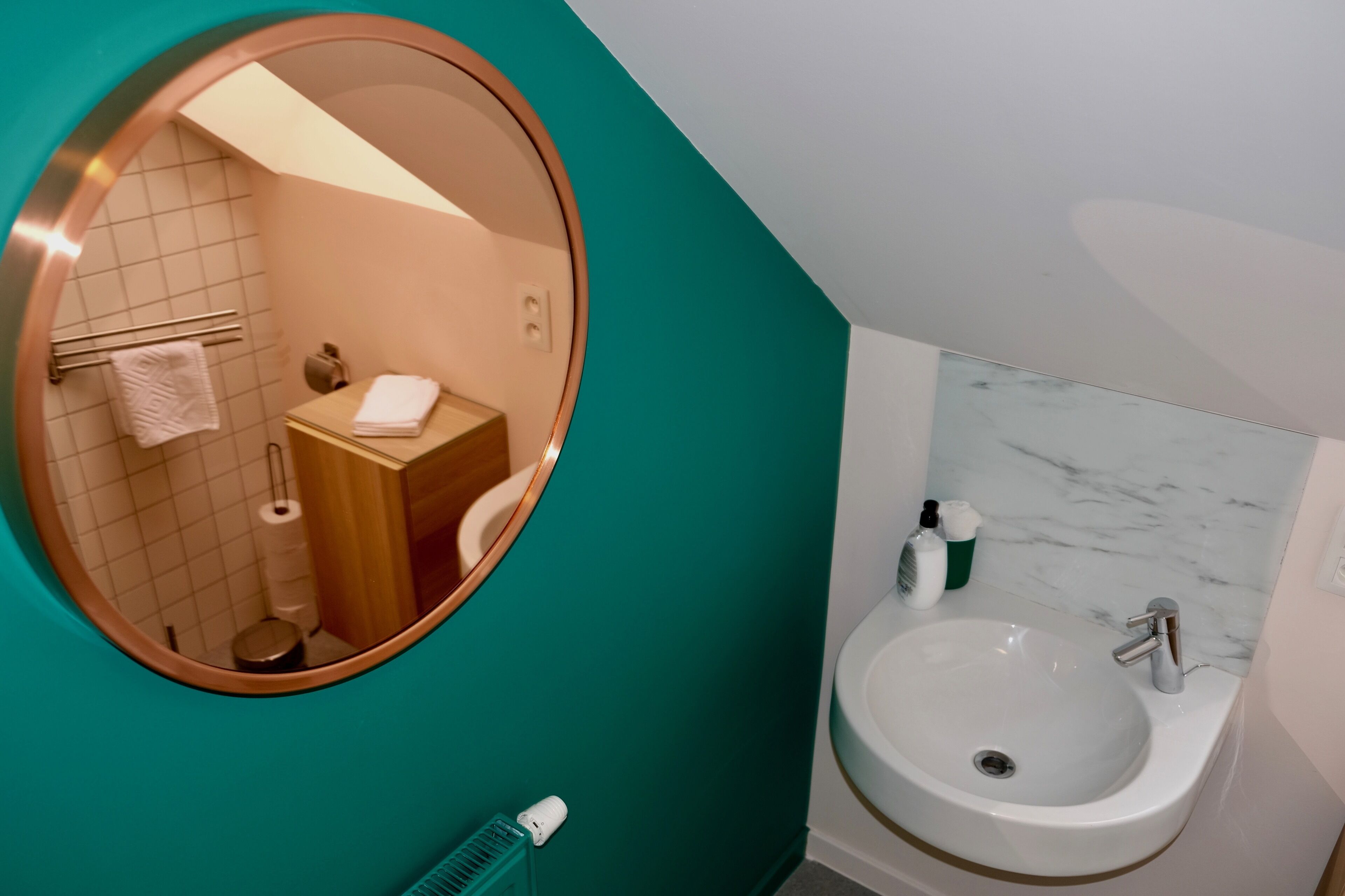 Une salle de bain avec un miroir rond, un lavabo, des toilettes et un porte-serviettes.