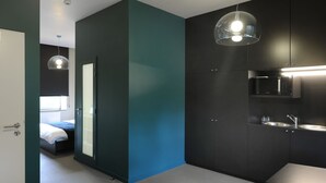 A modern bedroom with a large bed, a bathroom with a mirror and sink, and a kitchen area with a microwave. - Le Presbytère (Engis)
