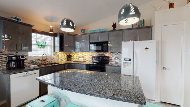 Una cocina moderna con encimeras de granito, electrodomésticos de acero inoxidable e iluminación colgante.