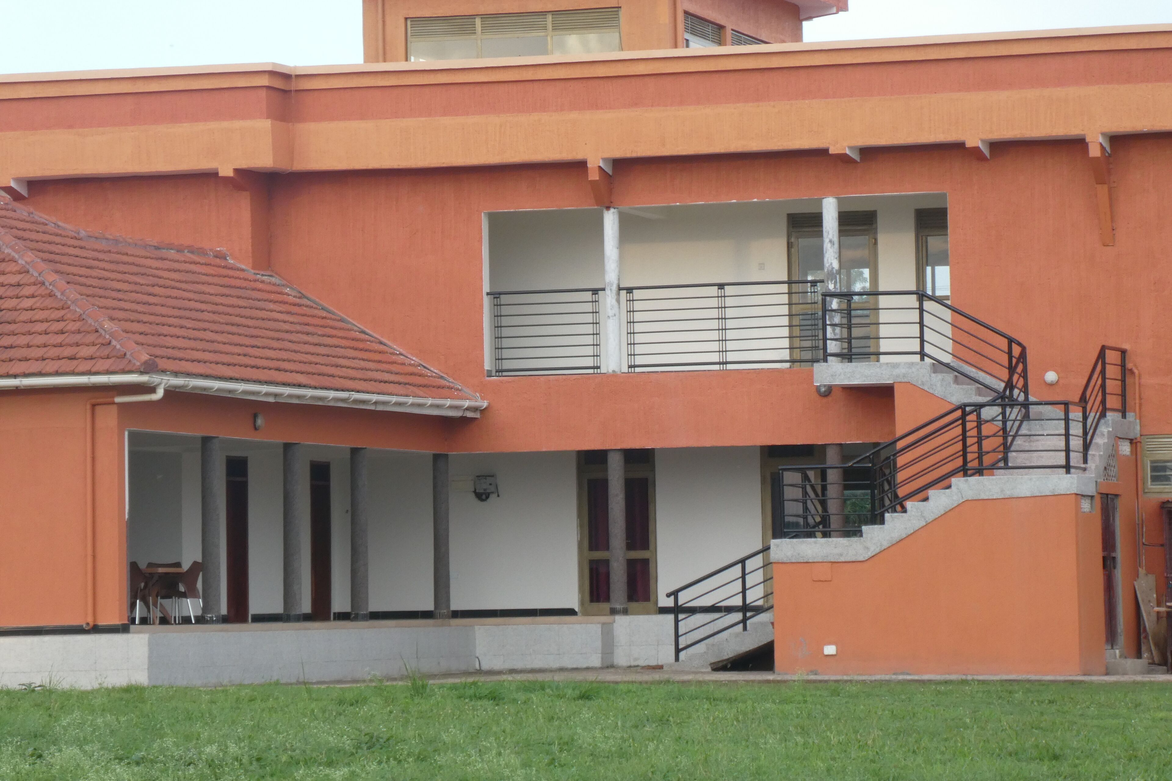Un edificio a più piani con facciata rosso-arancio, una zona relax all'aperto coperta e una scala che conduce a un livello superiore.