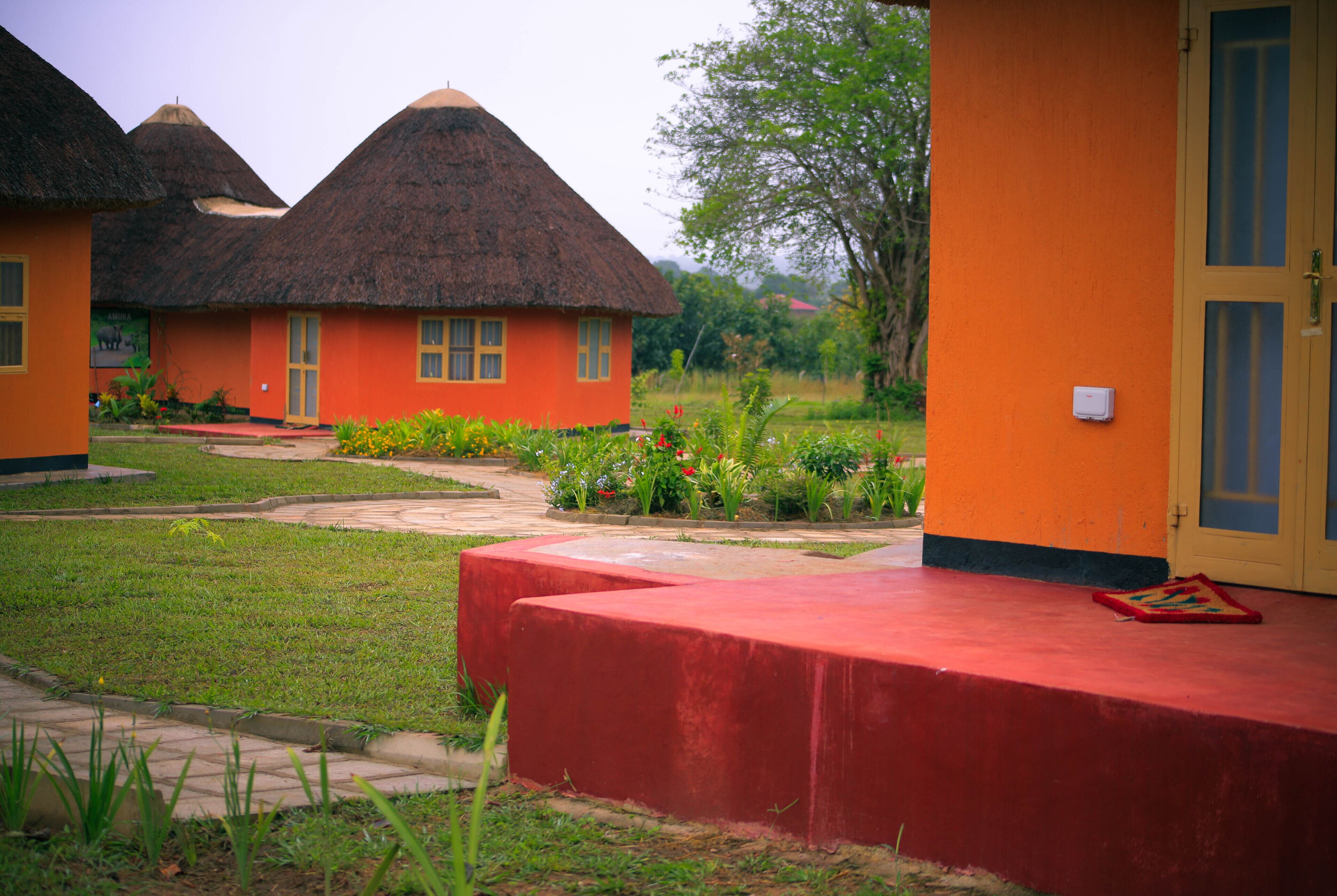 A building with thatched roofs and orange walls, surrounded by a garden with various plants and flowers.