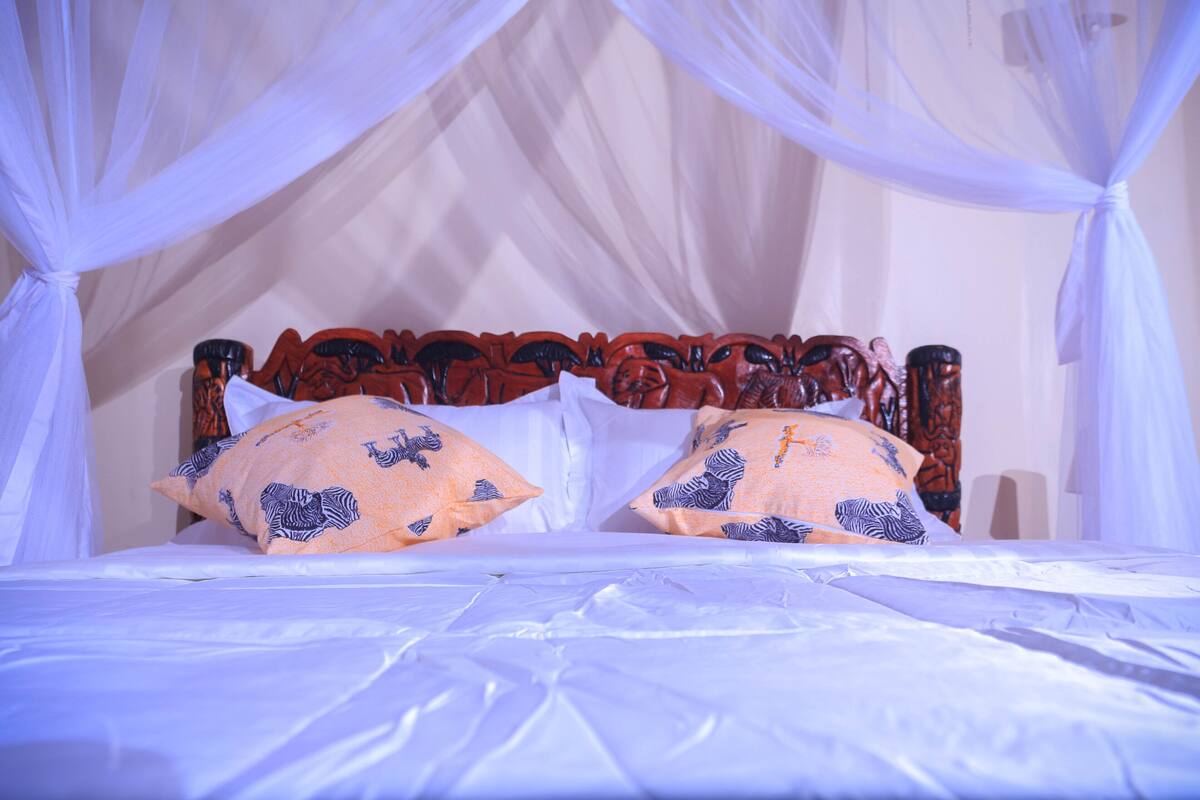 A bed with a canopy, two pillows with animal prints, and a wooden headboard.