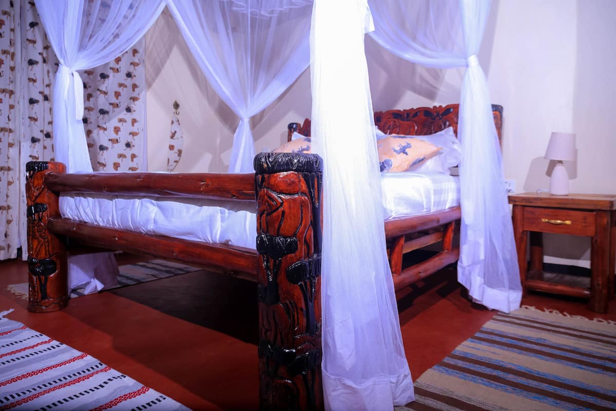 A wooden bed with a canopy, a nightstand with a lamp, and patterned curtains.