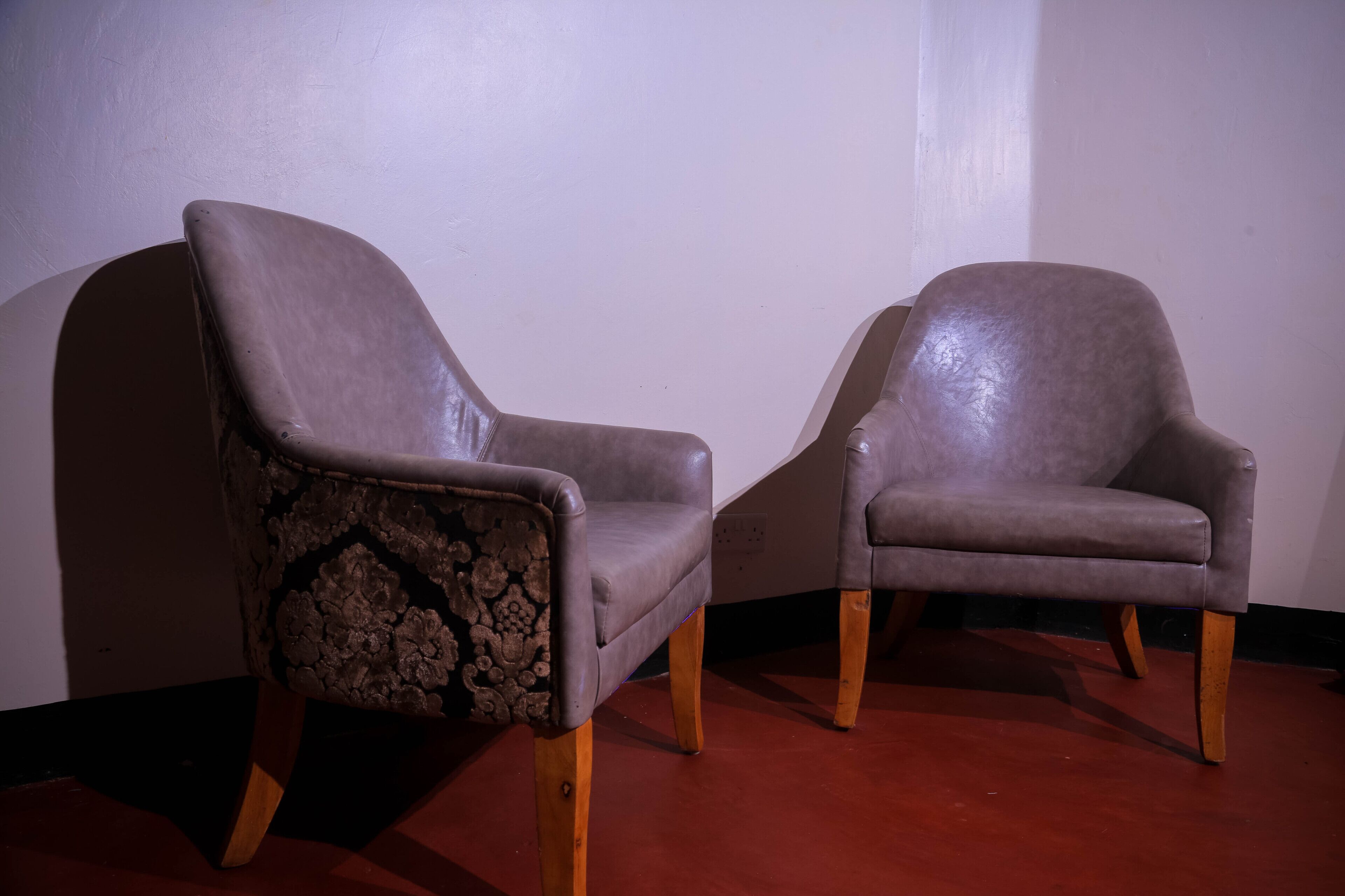 Two armchairs with wooden legs and a floral pattern on one armrest, positioned against a plain wall.