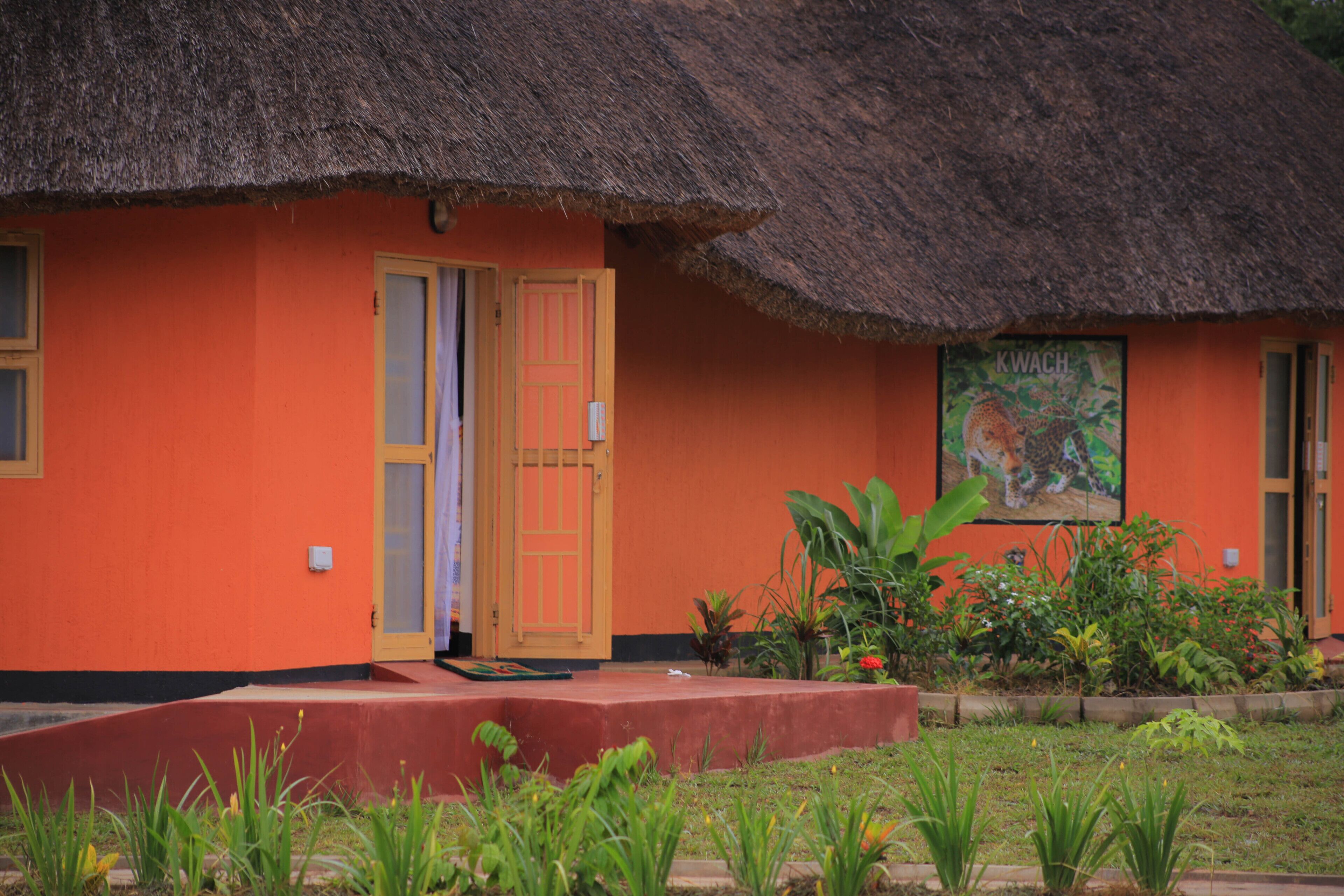 A thatched-roof building with an orange exterior and a wooden door.