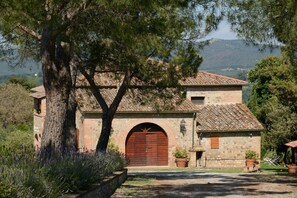 A rustic stone building with a large wooden door, surrounded by greenery and a mountainous backdrop. - Villa Alessandro (Citta della Pieve)