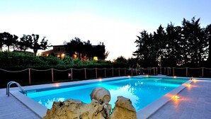 A rectangular swimming pool with a stone sculpture in the center, surrounded by a low stone wall and a metal fence. - Villa Alessandro (Citta della Pieve)