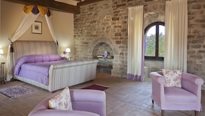 A bedroom with a large bed, two armchairs, a stone wall, and a window with curtains. - Castello Degli Arcieri (Gubbio)