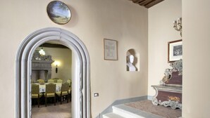 A hallway with a dining area visible through an archway, featuring a fireplace, dining table, and chairs. - Castello Degli Arcieri (Gubbio)